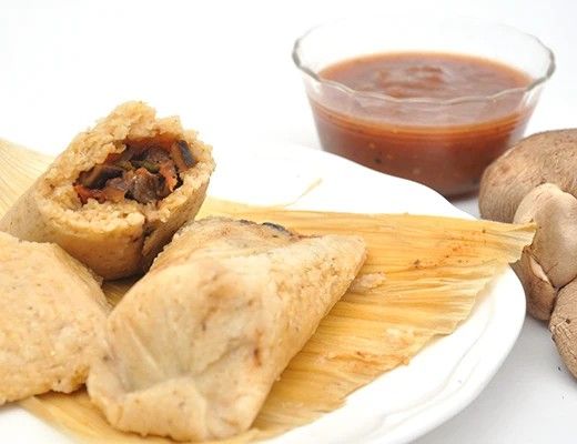 Plate of tamales with sauce and mushrooms on the side.