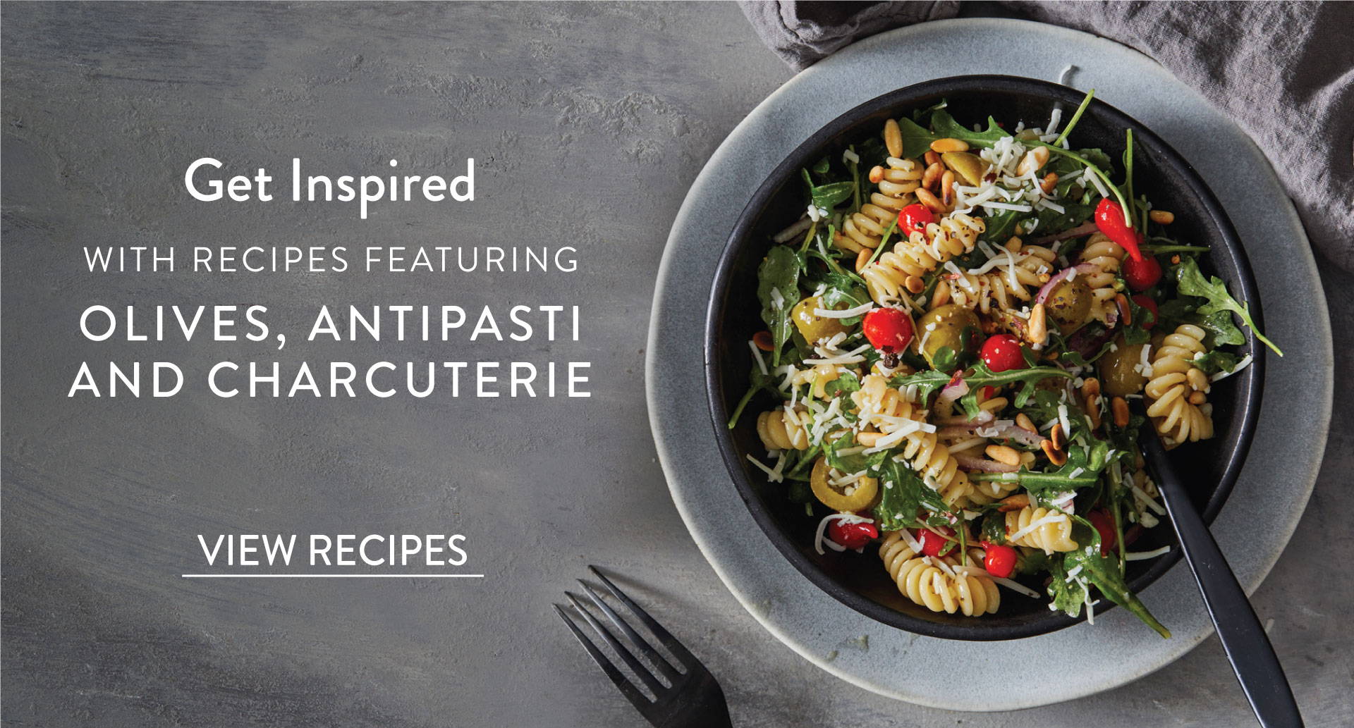 Fusilli pasta in a bowl mixed with olives, pepper drops and greens