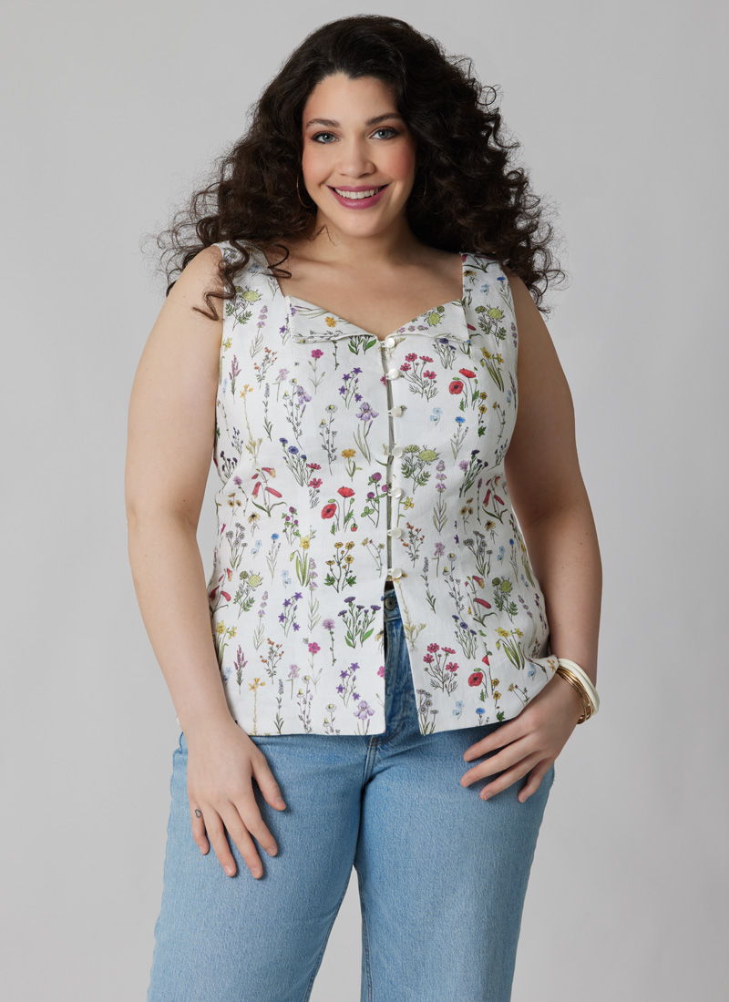 A woman in a floral top and jeans smiles at the camera.