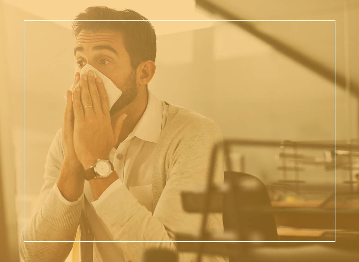 Man blowing his nose at his desk. Dust mites can cause sneezing, a runny or stuffy nose but bed bugs usually don’t.