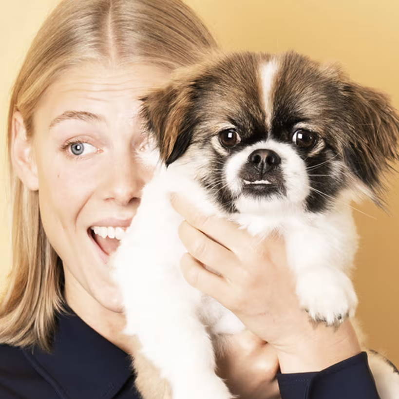 Une jeune femme qui tient un petit chien dans ses bras et présente peut-être une conjonctivite allergique.