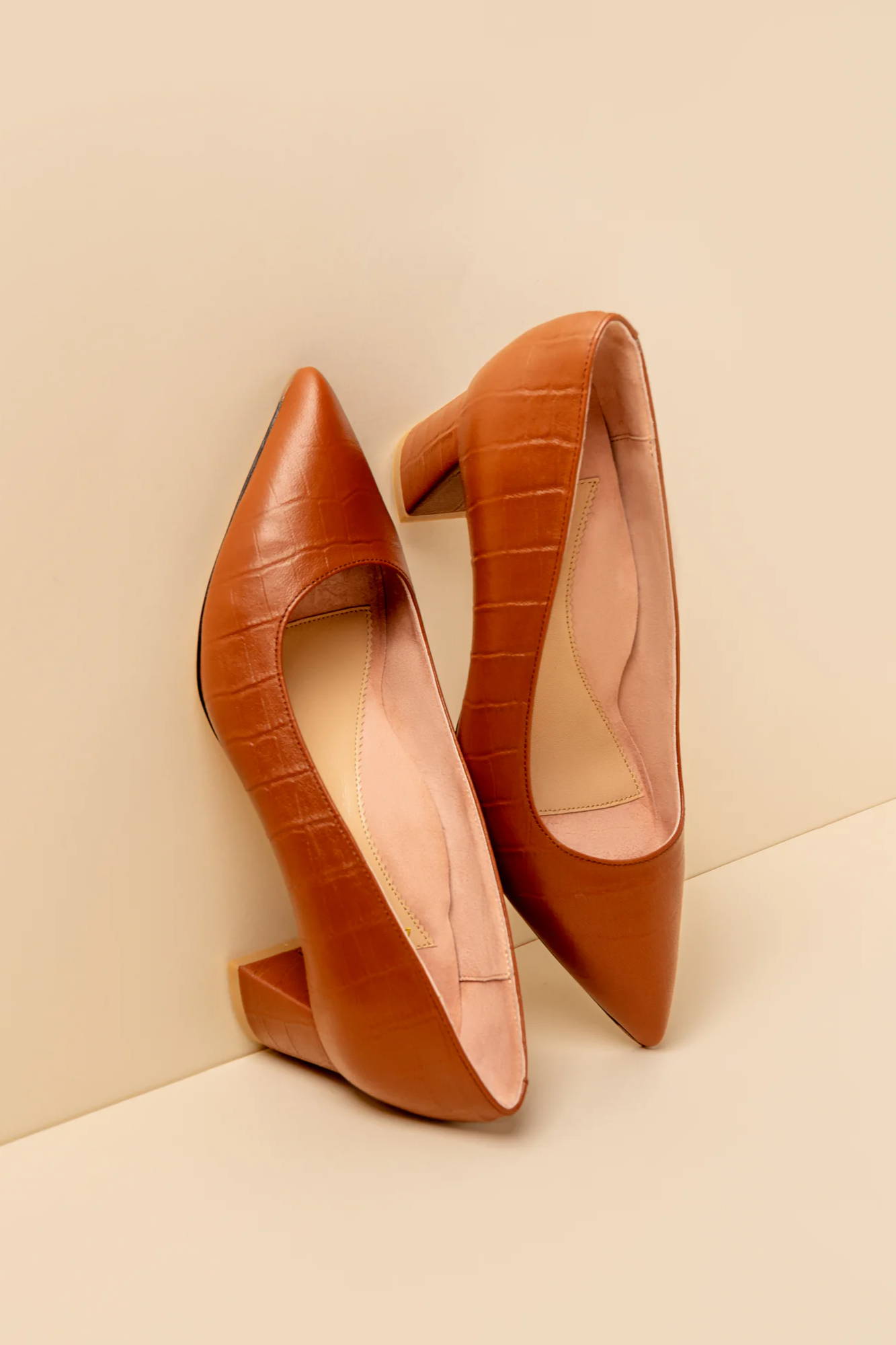 A pair of brown leather high-heeled shoes against a beige background.