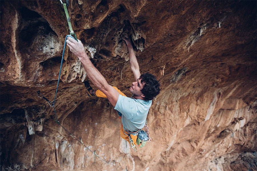 Ben rock climbing with a beautiful mountainscape in the background and blue sky with clouds