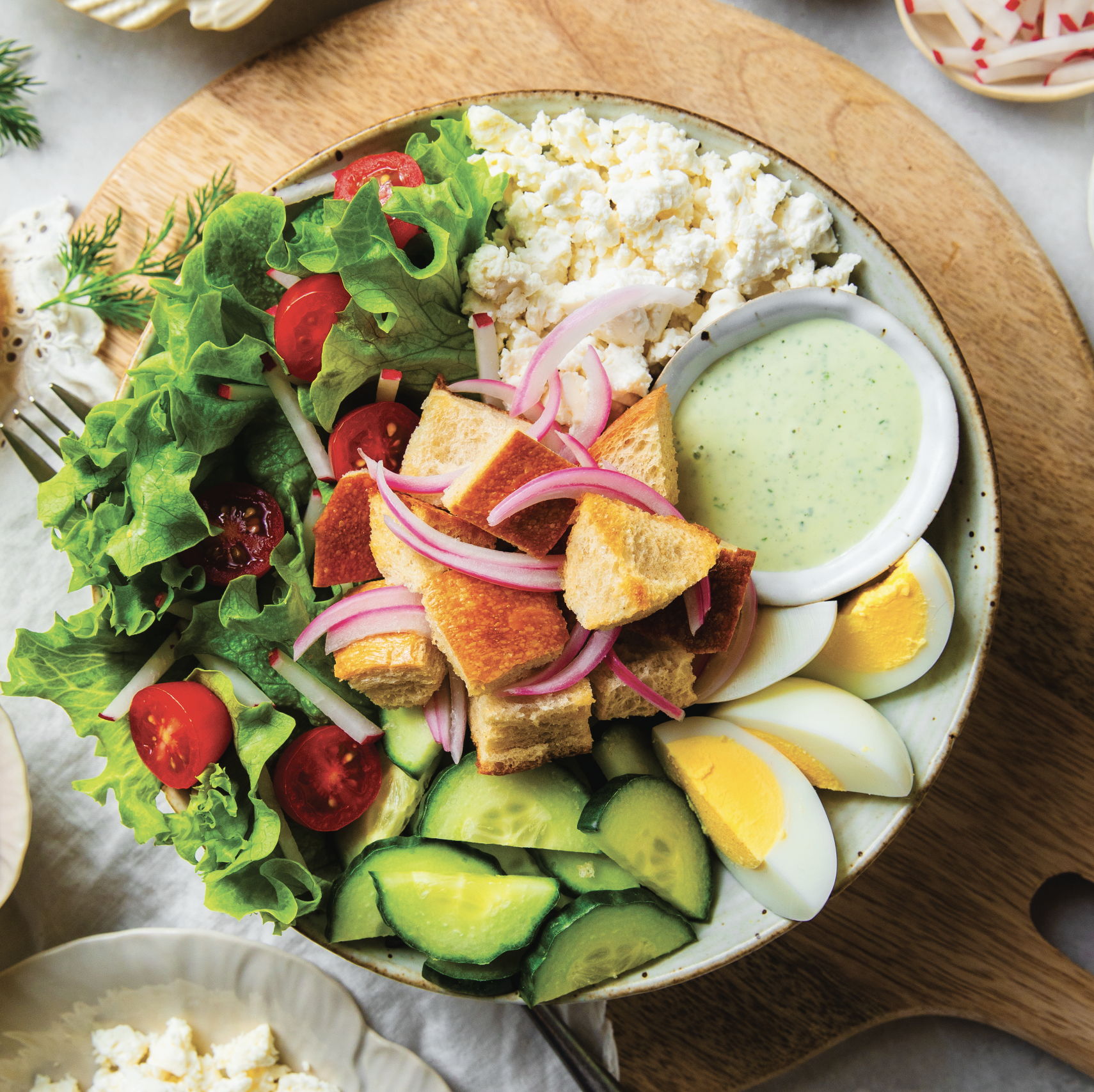 A colorful salad with greens, tomatoes, cucumbers, eggs, and dressing.