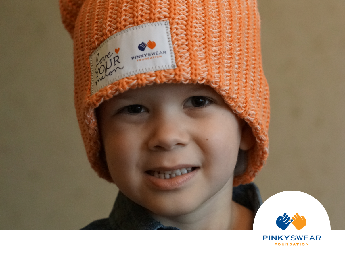 Small child wearing an orange beanie with a patch with Love Your Melon and Pinky Swear Foundation logos printed on