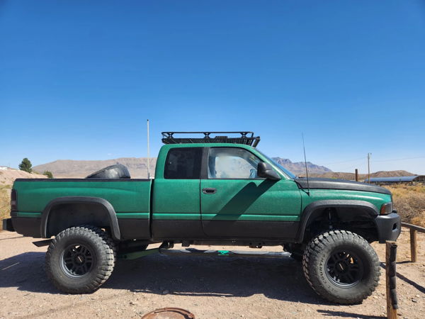 Side profile of lifted green Dodge Ram with Ironman off-road tires and spare tire in bed