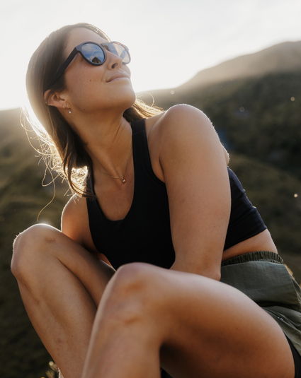 A woman in sunglasses sits outdoors, looking thoughtfully into the distance.