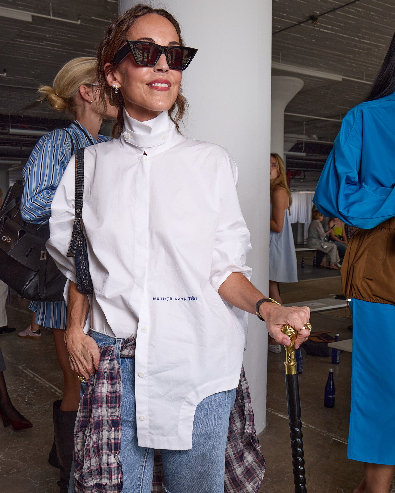Larissa Mills at Tibi new york fashion week runway show in oversized white shirt and sunglasses, holding a cane, smiling.