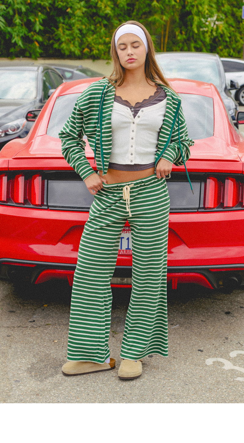 Young woman in striped outfit stands in front of a red car.
