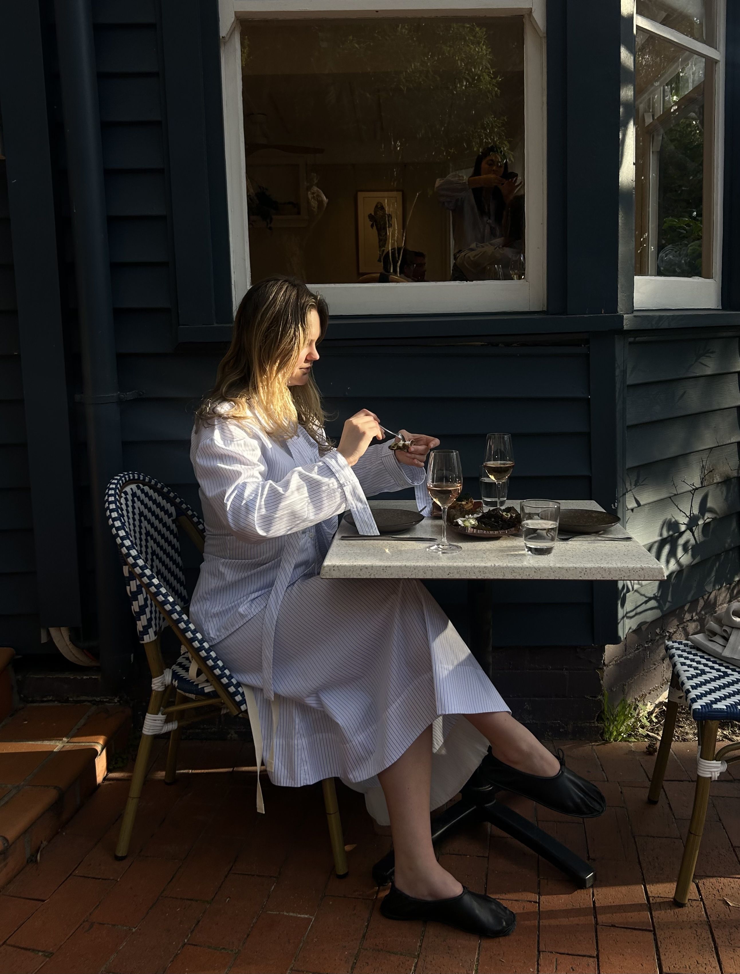 Woman in white robe enjoying a meal at an outdoor table.