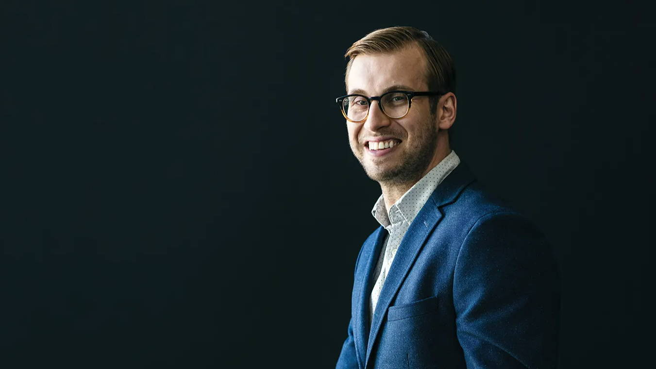 Portrait of Matt for Edify Edmonton. Matt is wearing a blue suit and smiles at a point to the left of the camera.