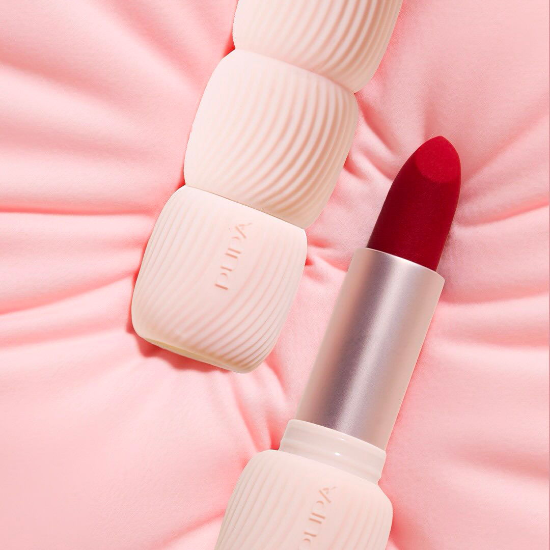 Red lipstick next to white containers on a pink background.