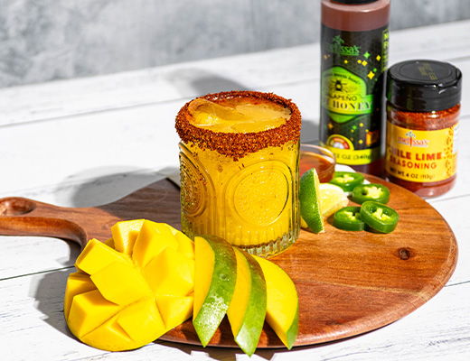 A glass of mango drink with mango slices and spices on a wooden board.