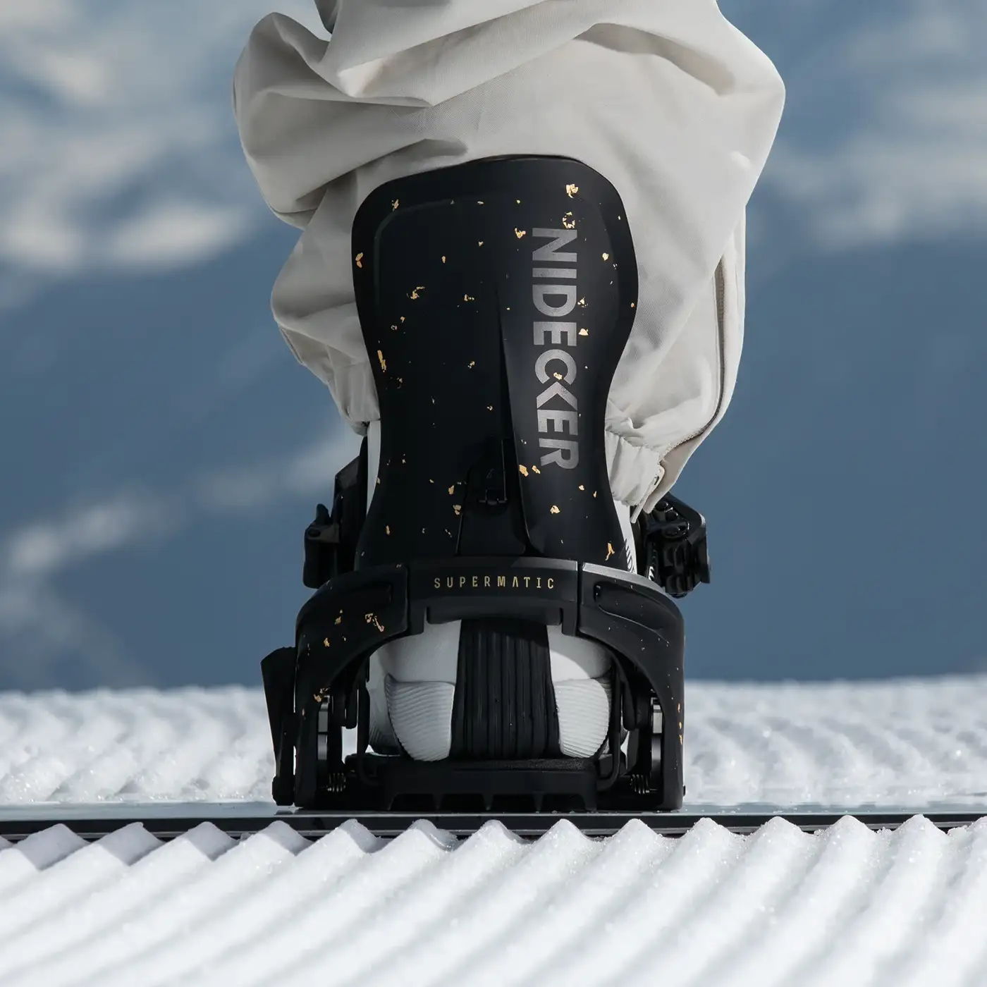 Snowboard boot secured on a snowboard with snowy mountains in the background.