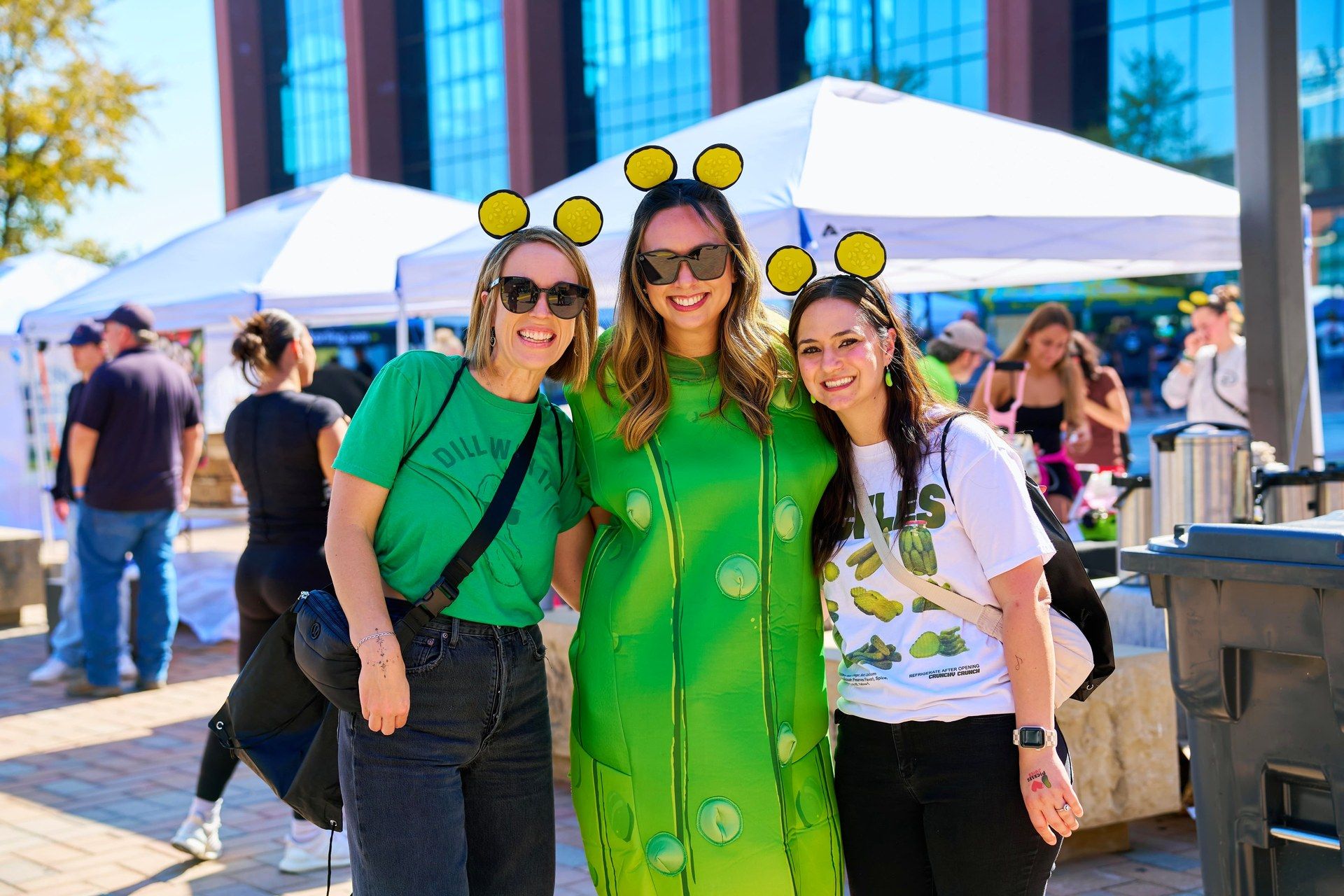 Three friends in pickle costume, pickle slice headbands, and pickle graphic tees pose together at The Big Dill, Globe Life Field and Texas Live!, Arlington 2025
