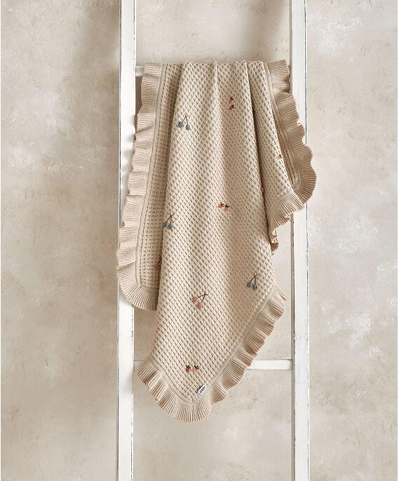 A decorative blanket hanging on a white ladder against a textured background.