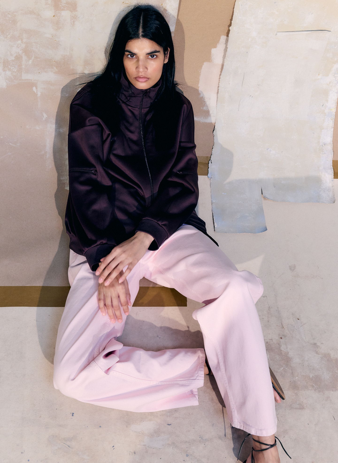 A person sitting in stylish outfit against a textured background.