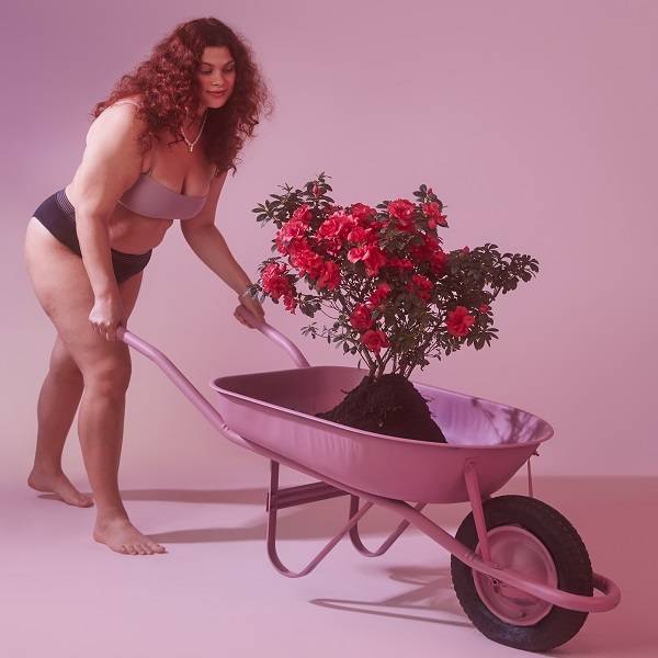 Modelo segurando uma carriola rosa com flores em cima 