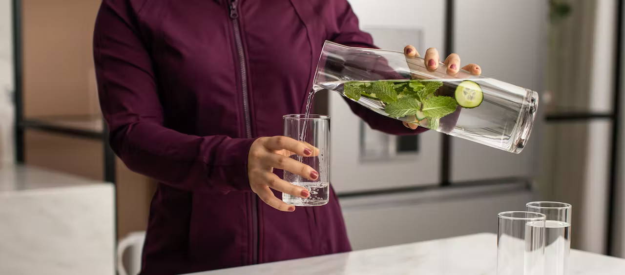 Woman pouring mint-infused water into a glass in front of Modern Glass refrigerator
