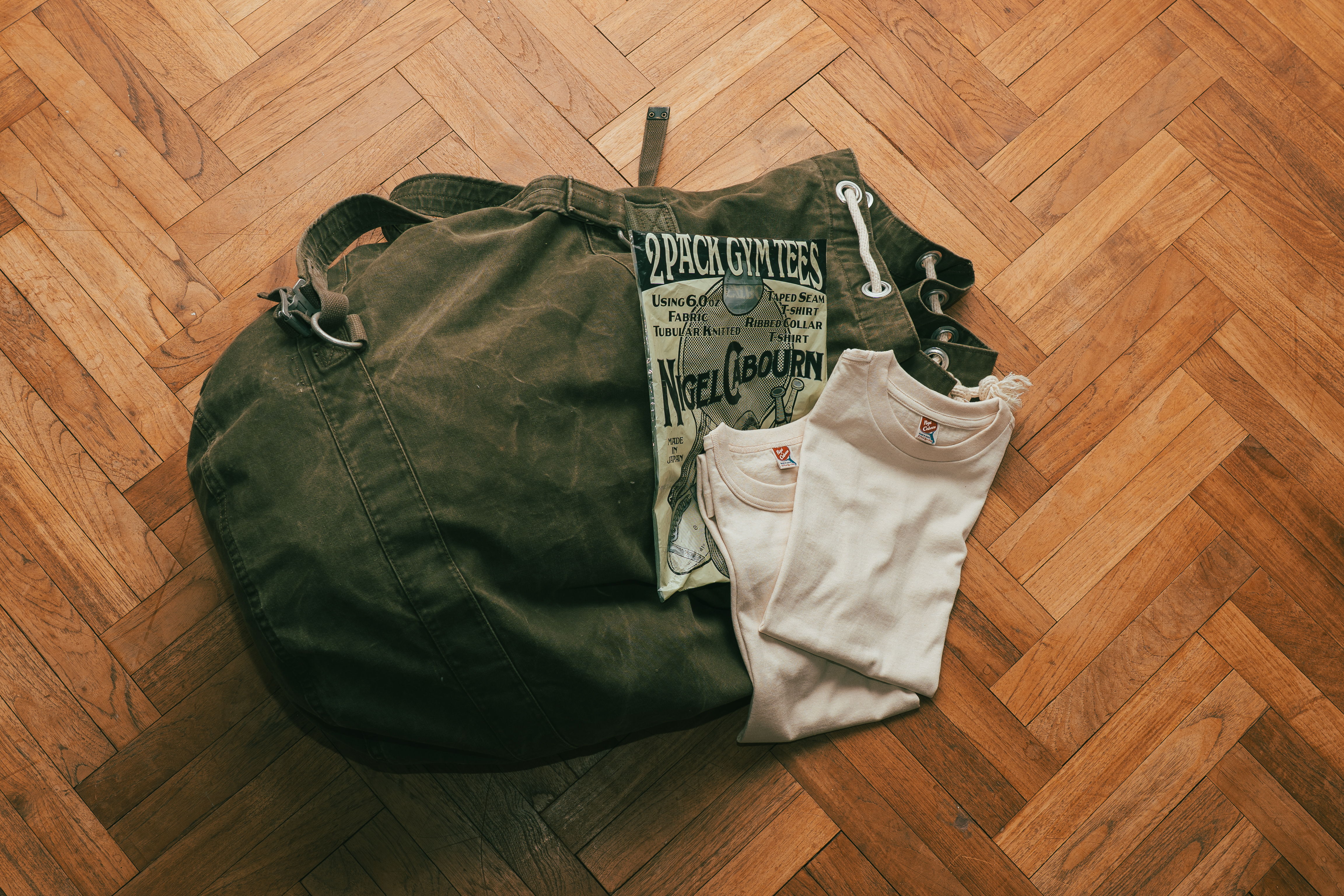 A green duffel bag with folded clothing on a wooden floor.