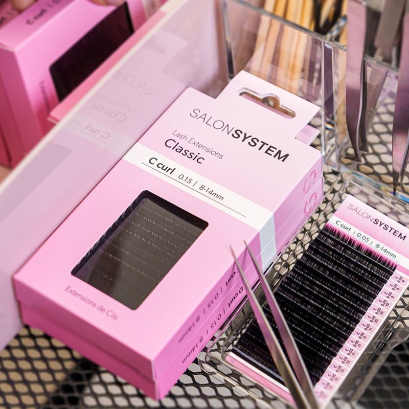 A box of eyelash extensions with tweezers on a mesh surface.