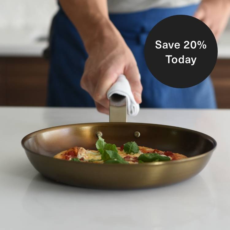 A chef holds a well-seasoned Misen Carbon Steel Pan with a kitchen towel around the handle. The pan contains a small pizza.