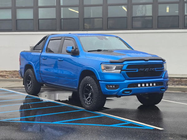 Front three-quarter view of blue RAM 1500 with off-road wheels and bed roll bar on wet parking lot
