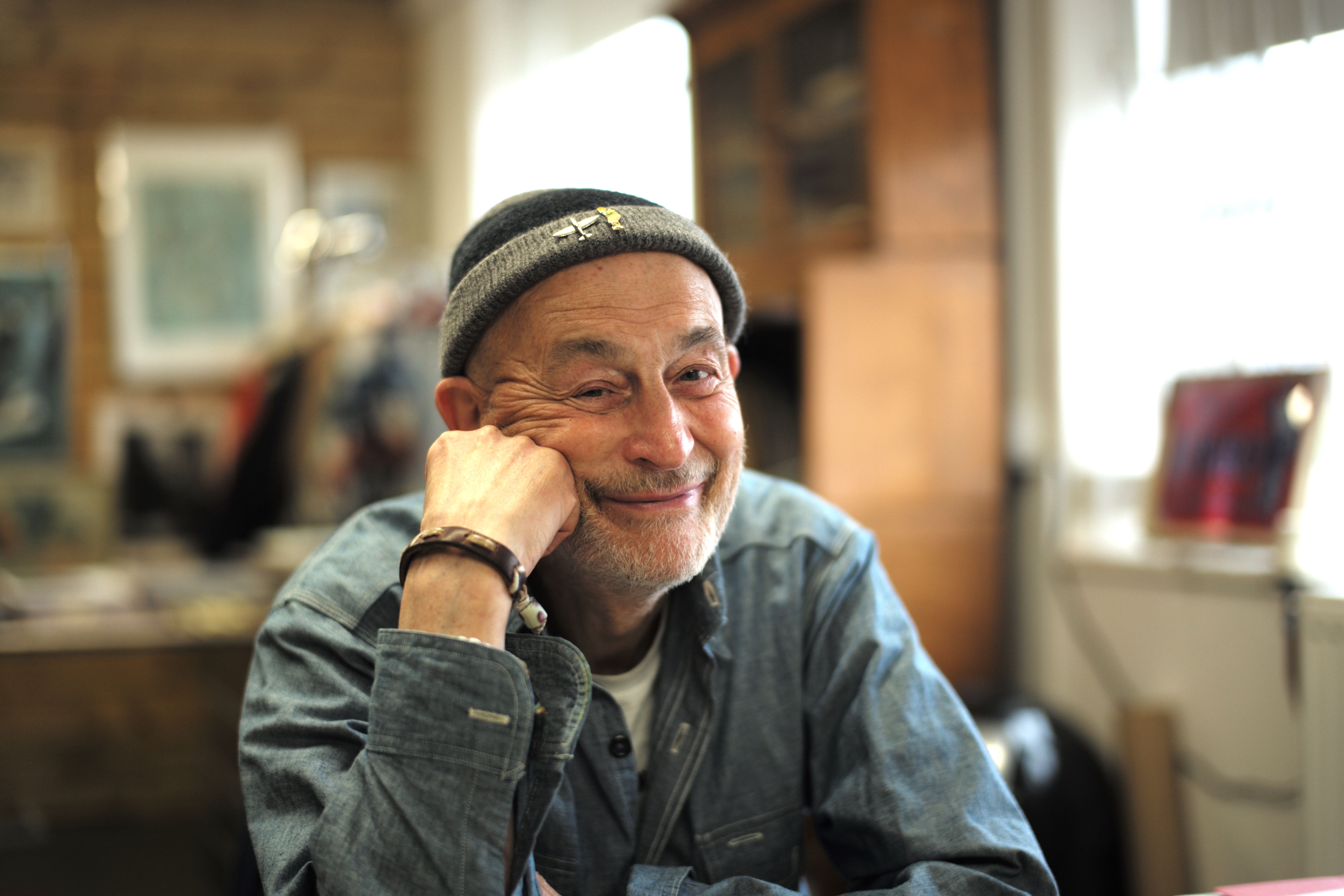 Smiling older man in a hat, sitting at a table in a cozy room.