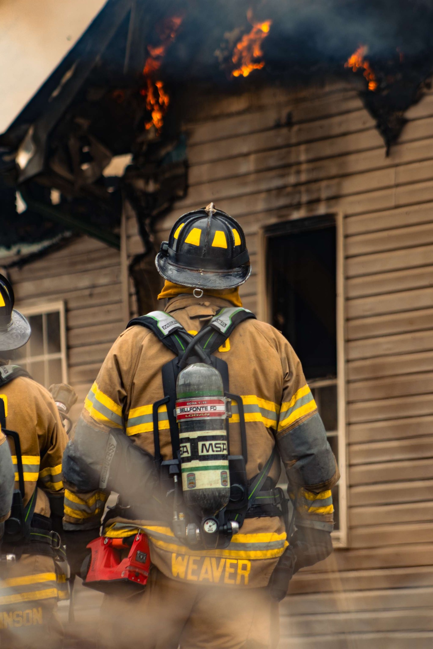 Firefighters responding to a house fire with flames visible.
