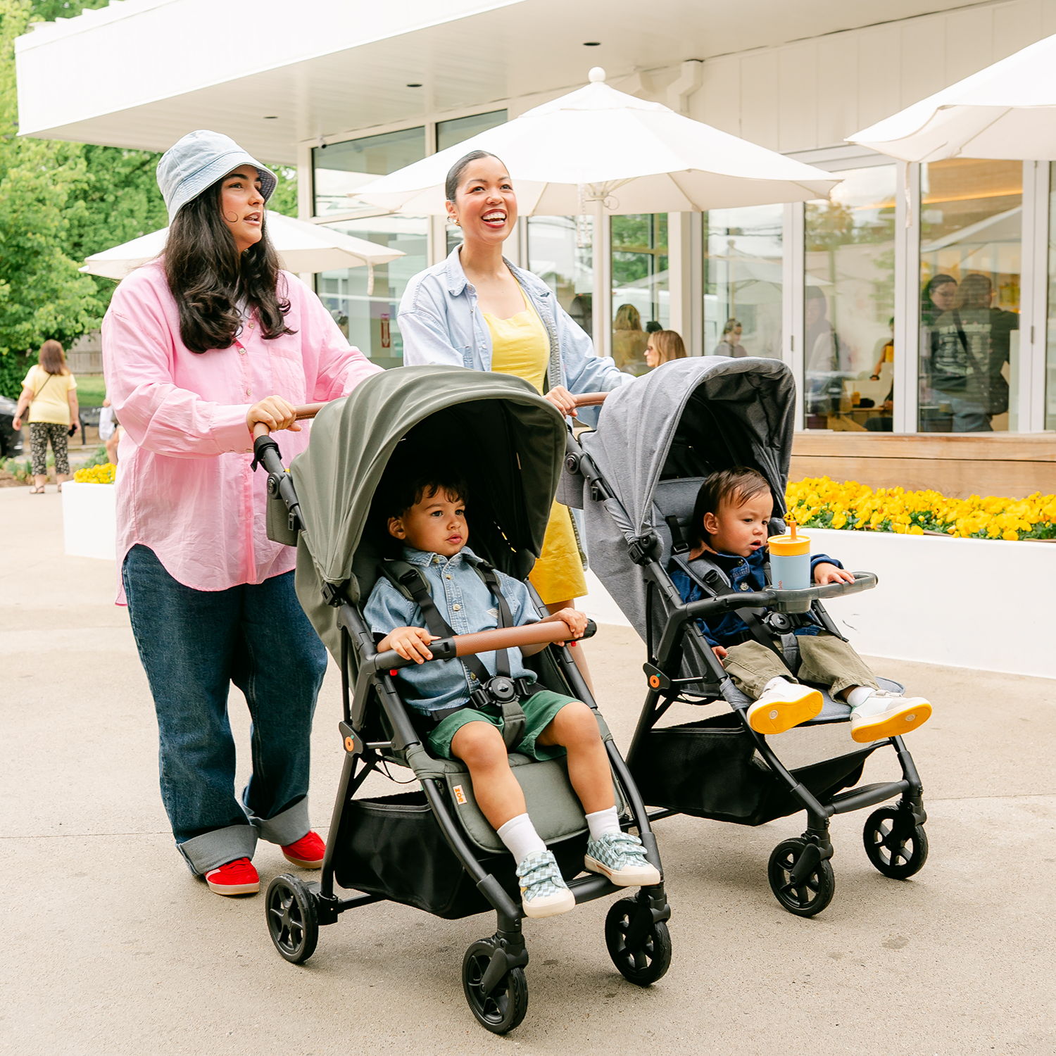 Two women pushing strollers with children in a park setting.