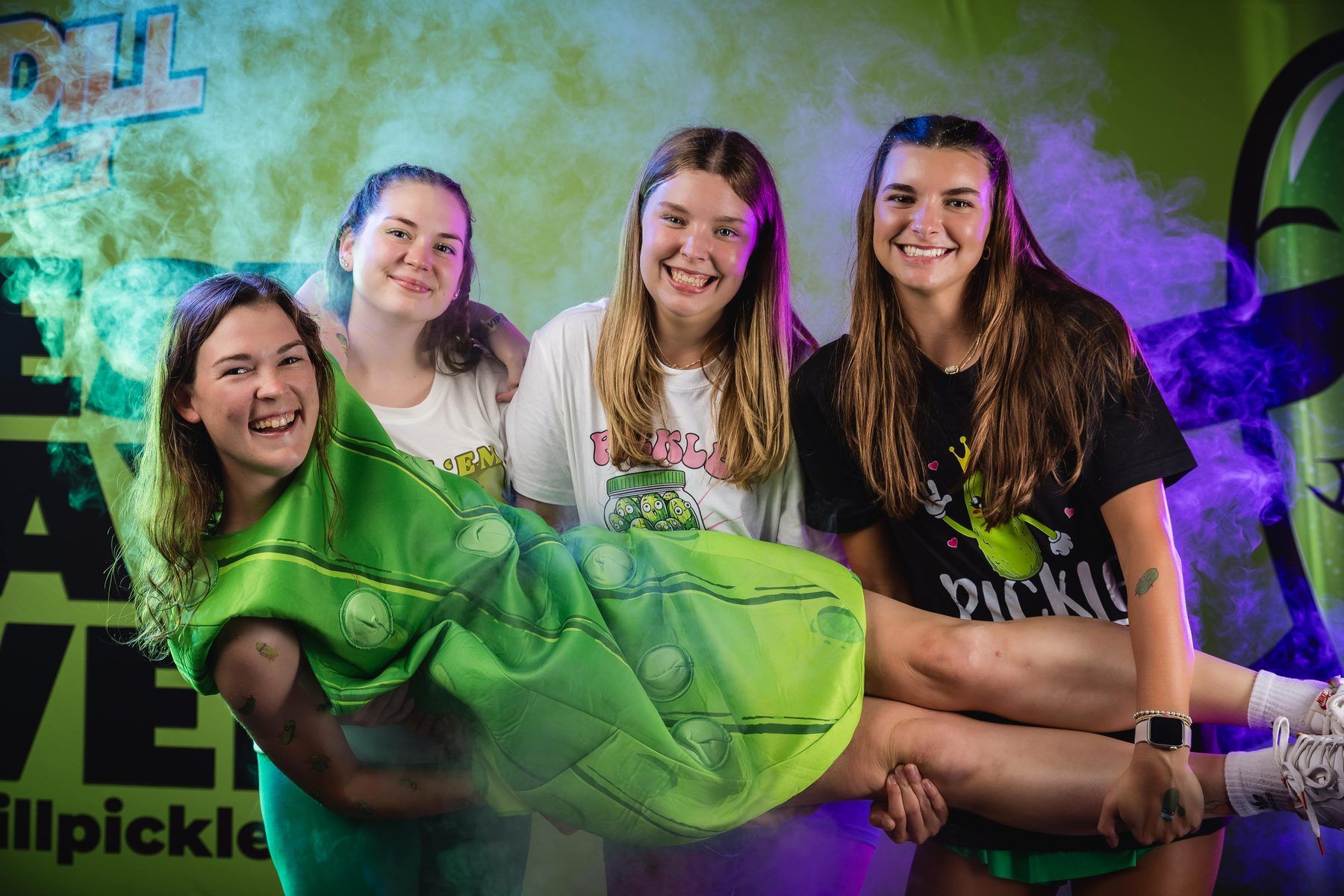 Four friends posing with one held in a pickle costume at the photo booth at The Big Dill.