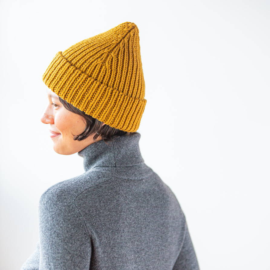 Kaya models a hand knit ribbed watchcap in Brooklyn Tweed Arbor Lodge chunky weight yarn against a white wall