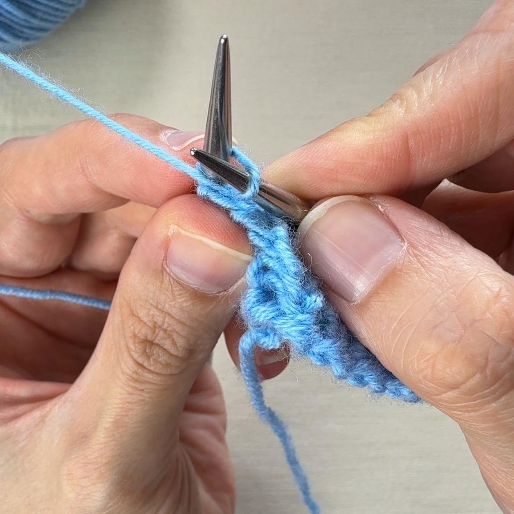 Linksverschränkt stricken: Die rechte Nadel sticht von hinten in die linke Masche ein.