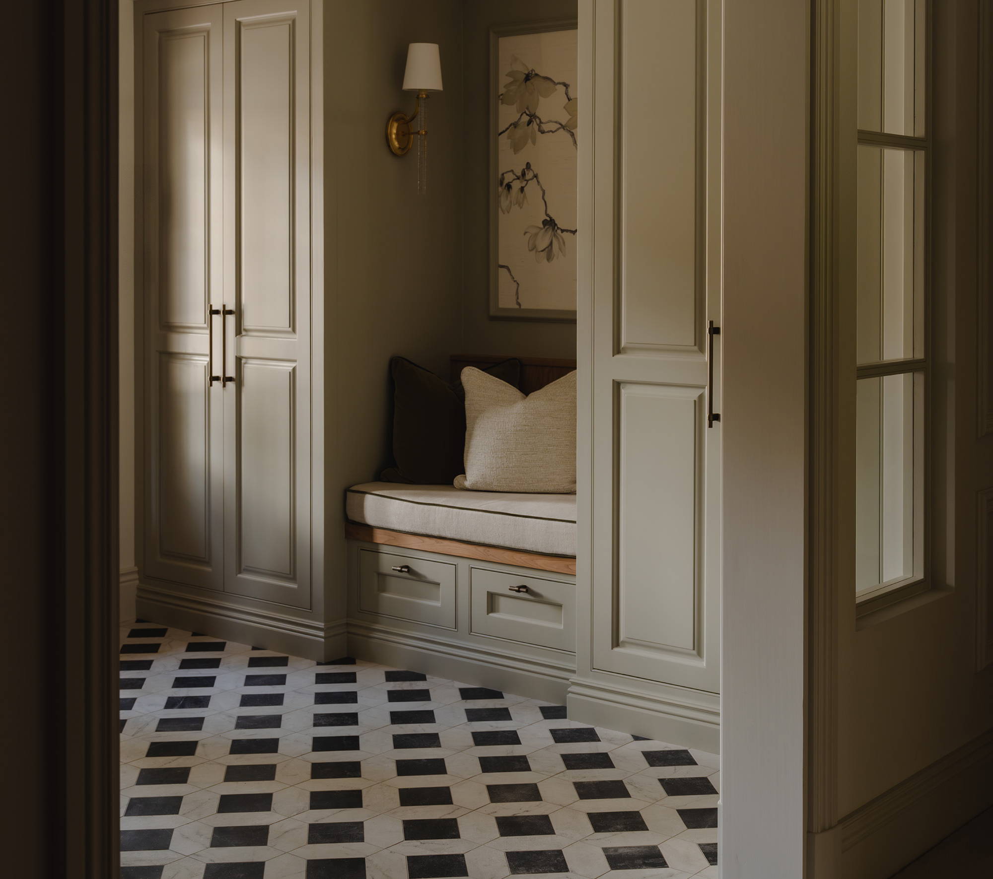 Luxurious mudroom design by Isla James Interiors with taupe cabinetry, brass hardware and black and white tiled flooring