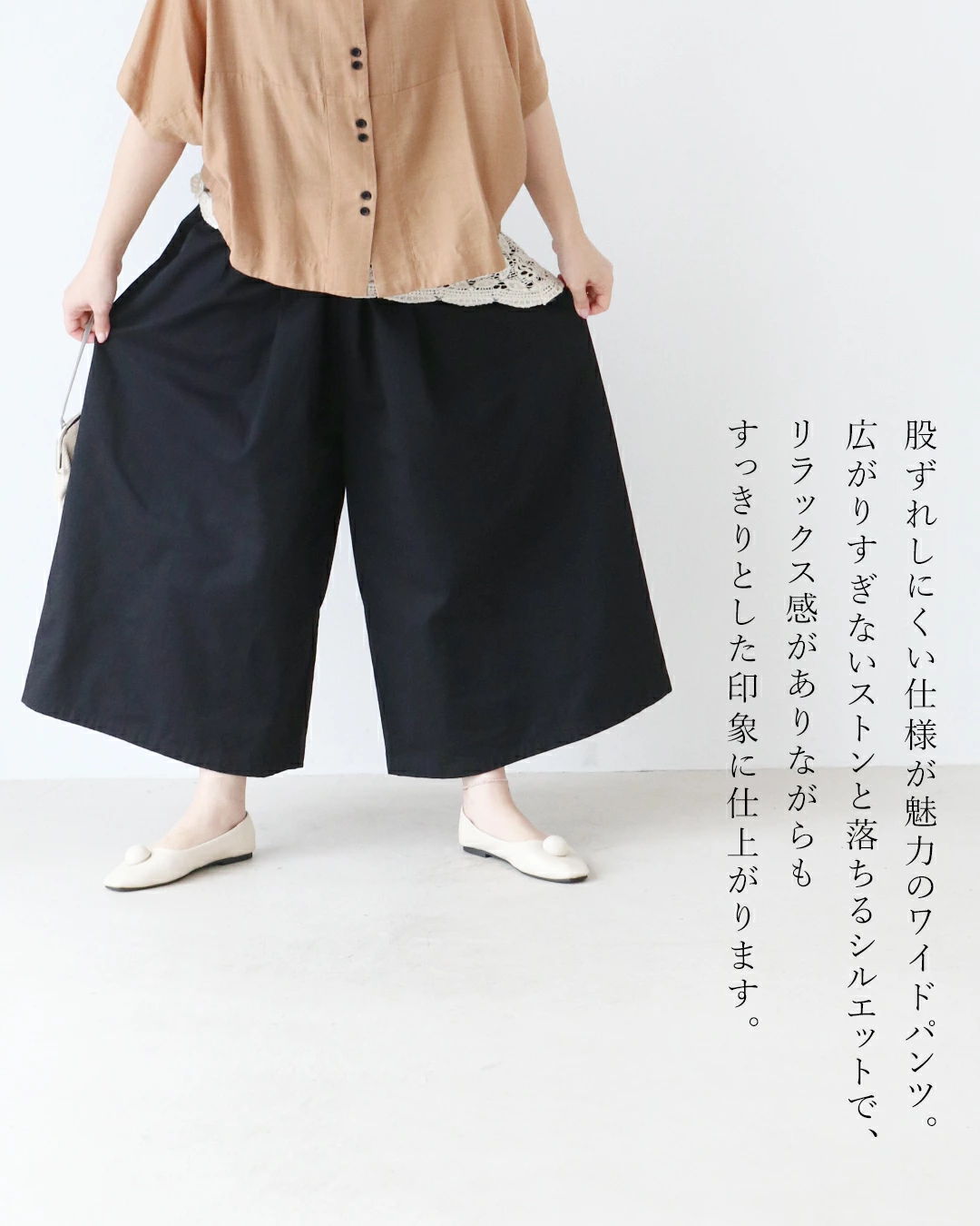 Person wearing a brown top and wide black pants, standing on a white background.