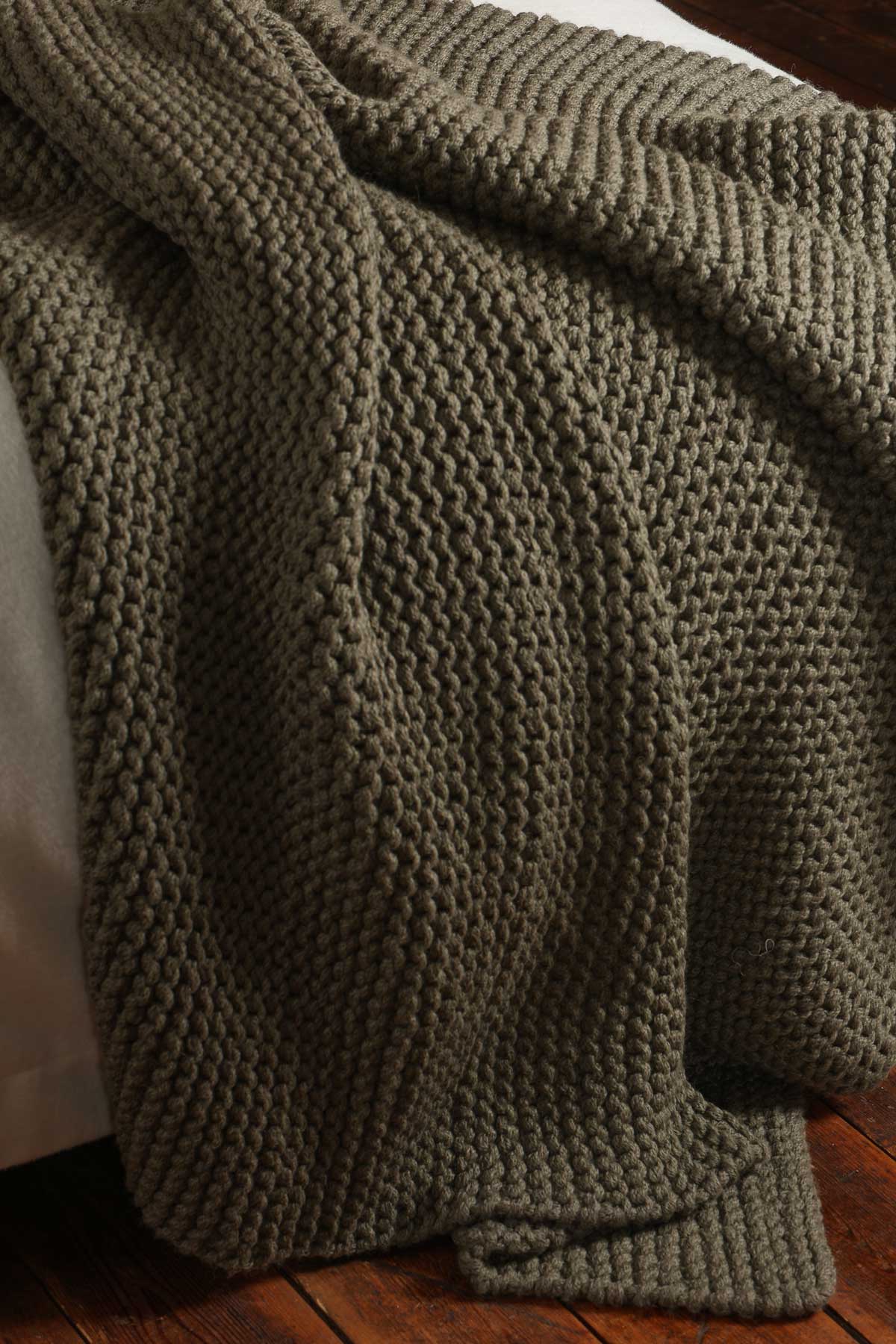Cozy knitted blanket draped over a bed with wooden flooring.