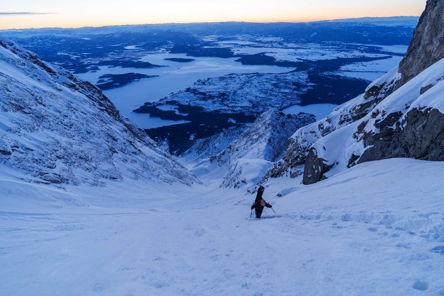 Person climbing a snowy slope with mountains and valleys in the background.