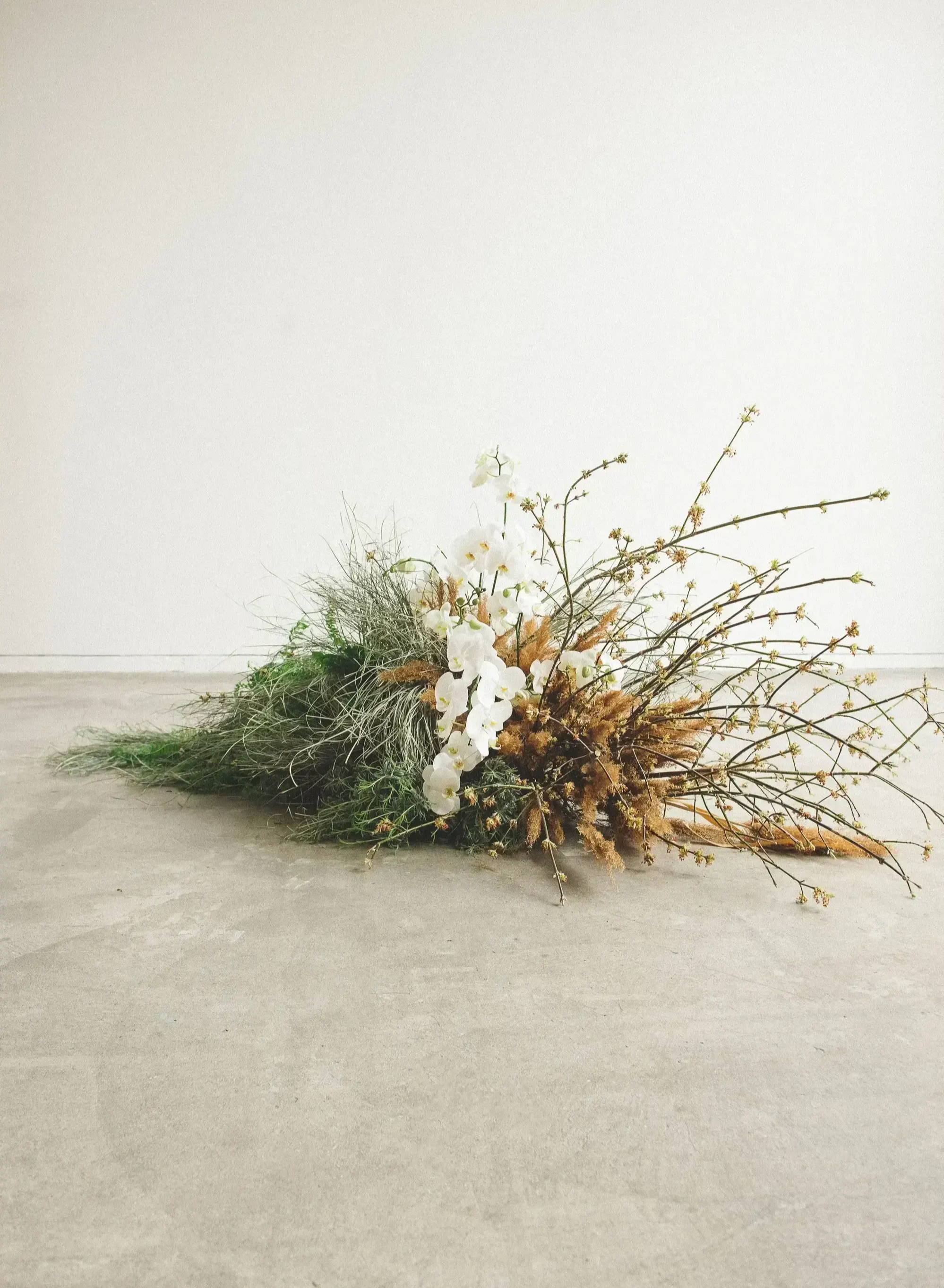 dried grass and twig installation on floor with white orchids