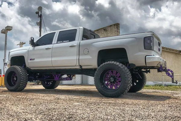 Side and rear three-quarter view of Ash's white 2015 Chevy Silverado 2500HD with purple suspension and black wheels, install photo 6