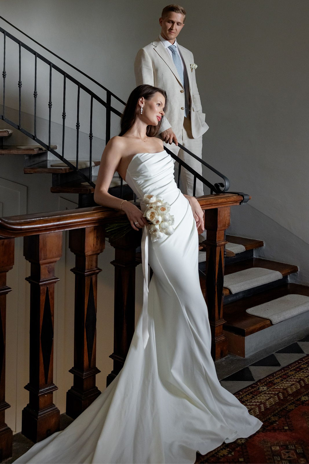 A bride and groom posing on a staircase in elegant attire.