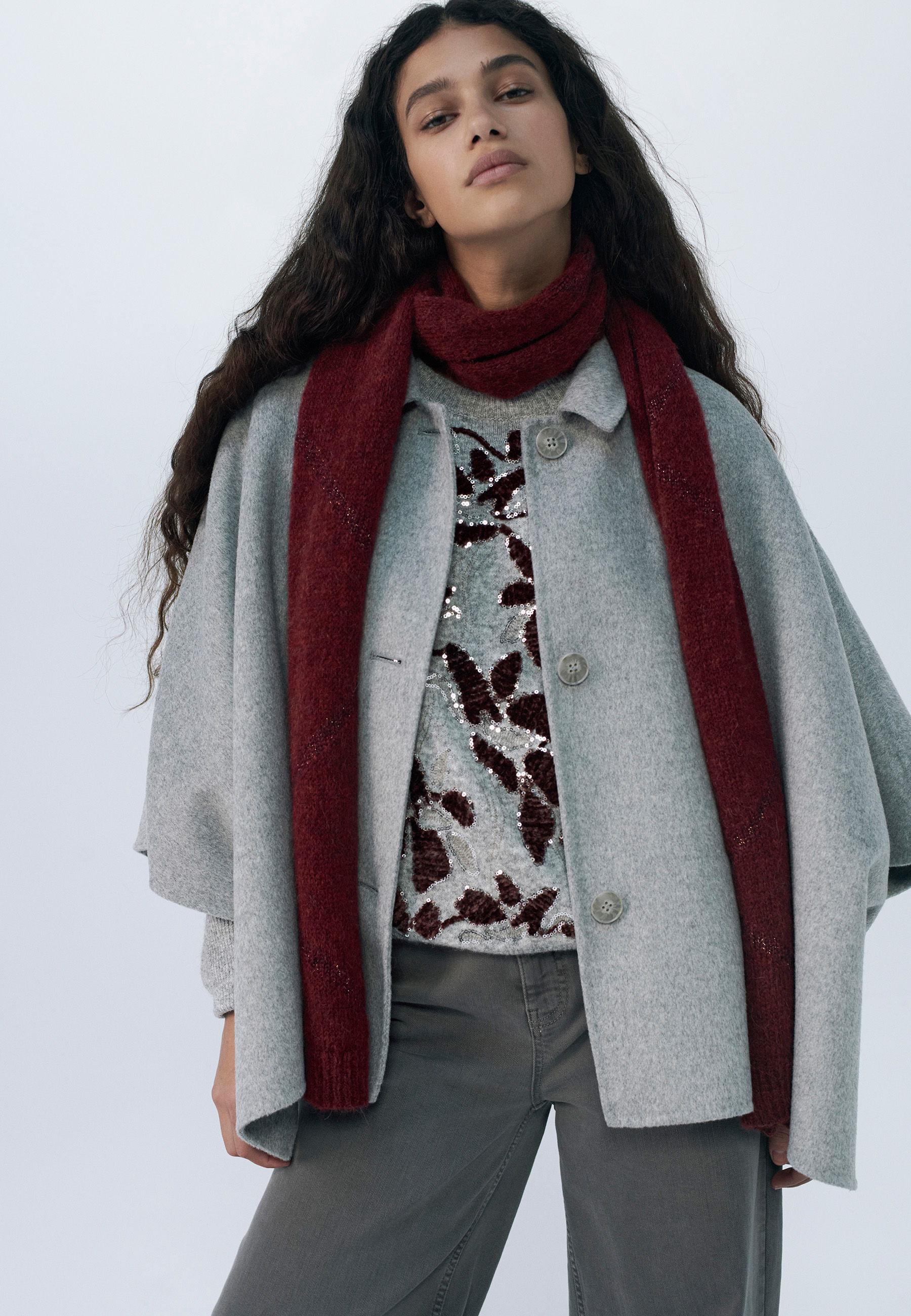Woman in a gray coat and red scarf, posing confidently.
