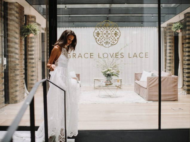 Novia frente a la fachada de una tienda de novias Grace Loves Lace