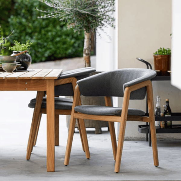 Premium outdoor dining chair with teak frame and gray performance fabric beside a wood patio dining table.