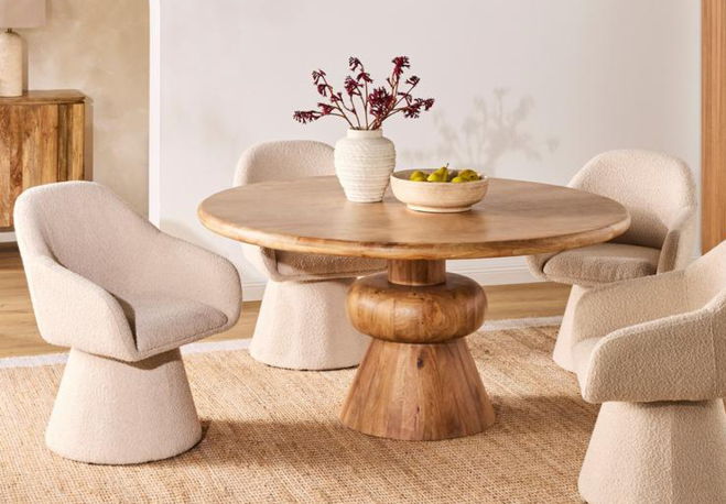 A round wooden dining table with soft, beige chairs and a vase of flowers.
