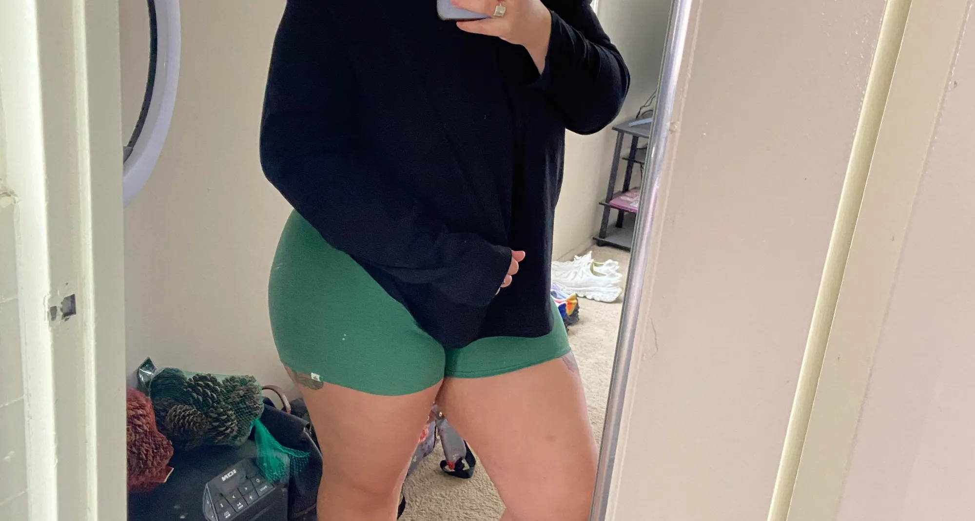  woman taking a mirror selfie with her phone wearing a black sweatshirt and green boy shorts