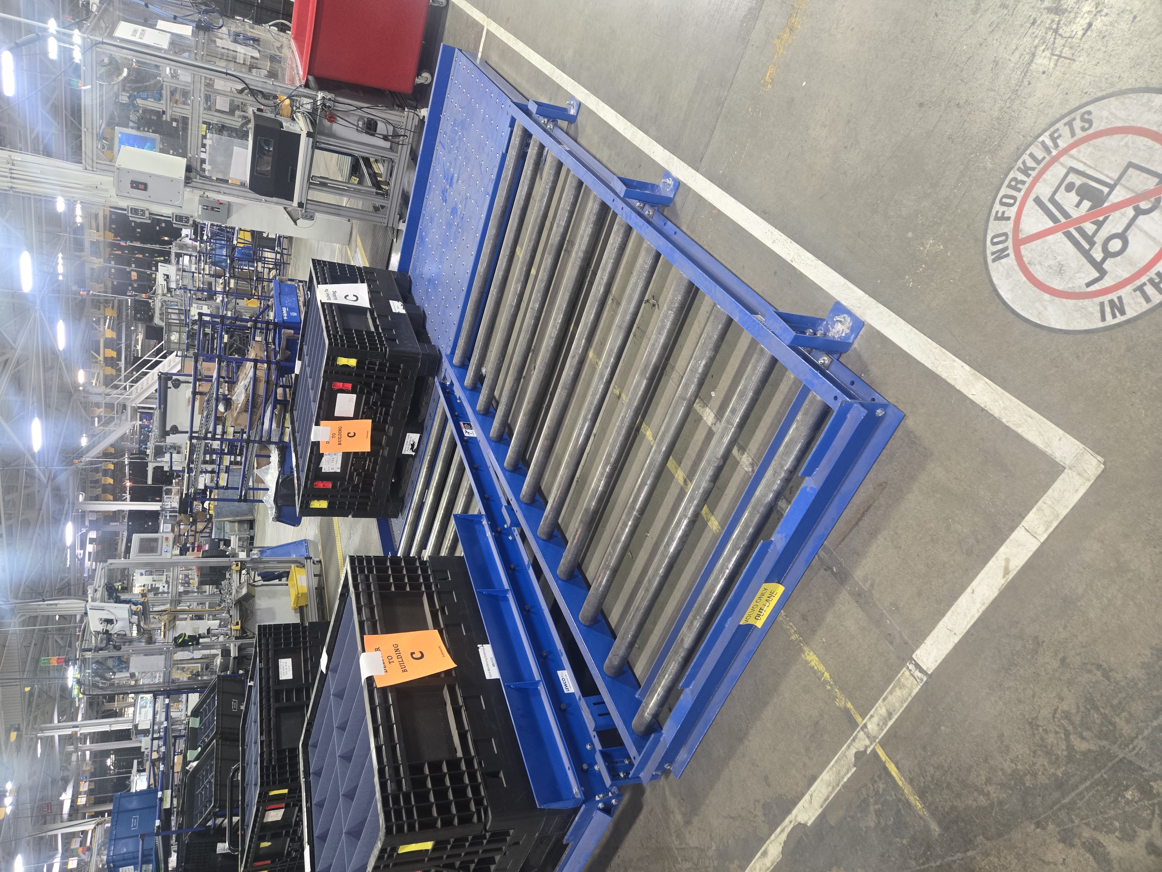 Industrial warehouse with blue roller conveyor and black storage bins.