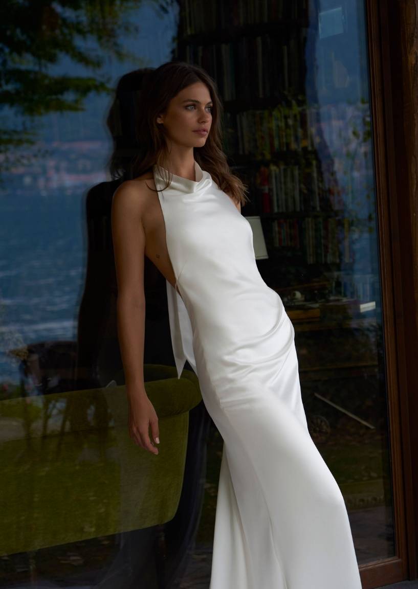 Modell im Goldie-Kleid lehnt an einem Glasfenster