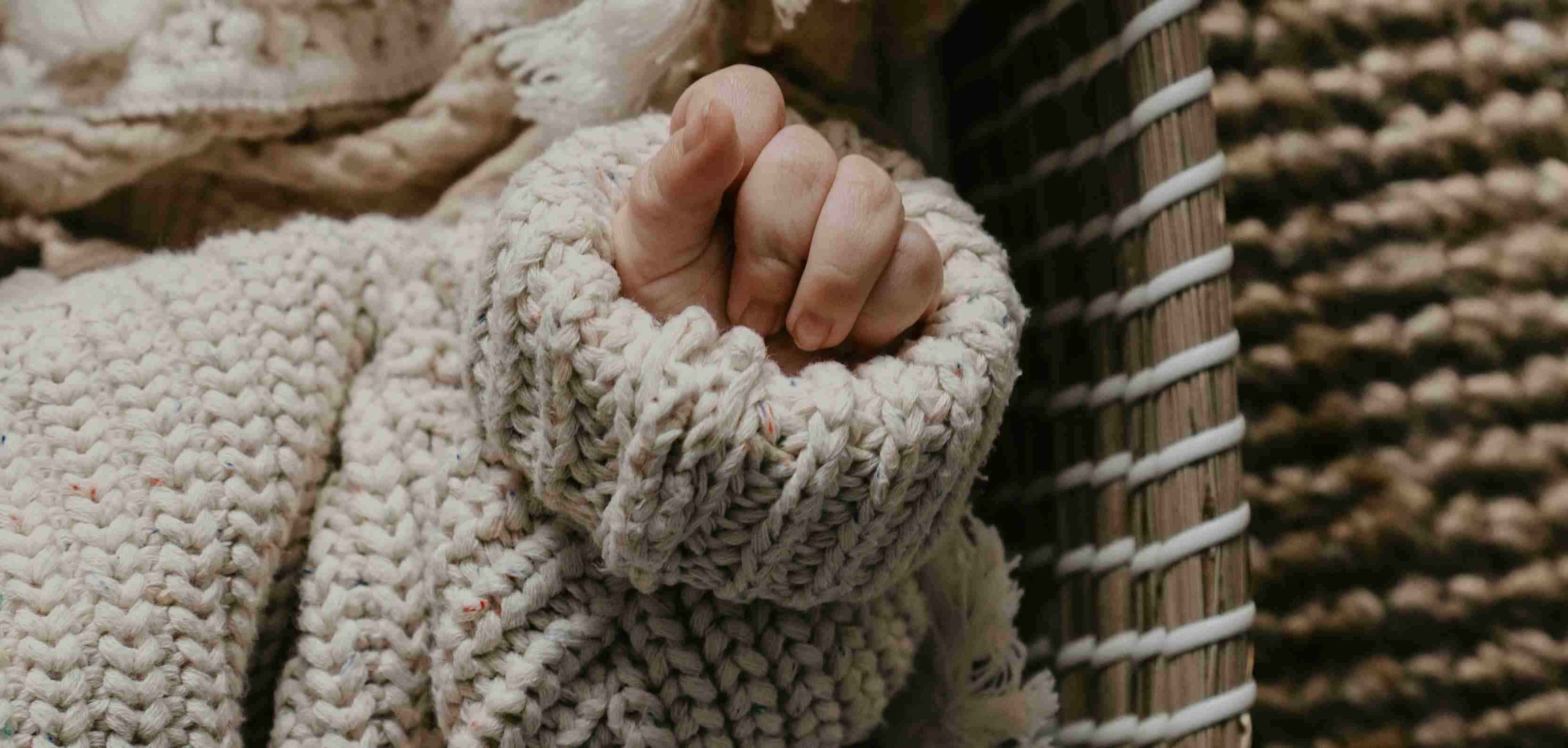 Detailaufnahme einer Babyhand, die aus einem gestrickten Ärmel herausschaut.