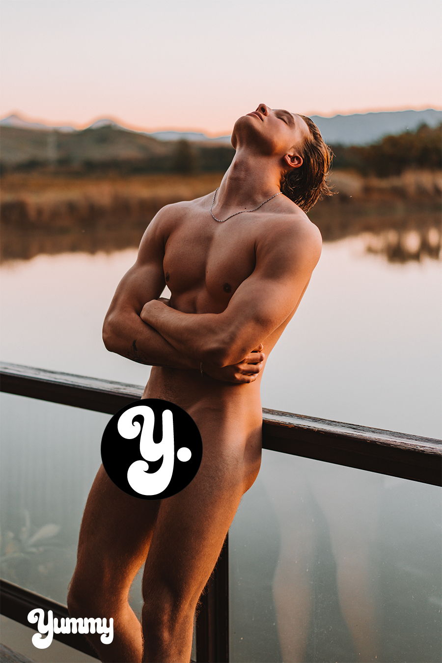 Man posing by a lake during sunset, partially obscured by a logo.