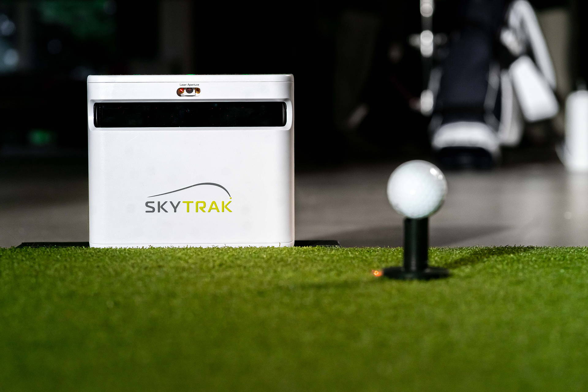 SkyTrak+ unit on a golf hitting mat behind a golf ball on a plastic tee